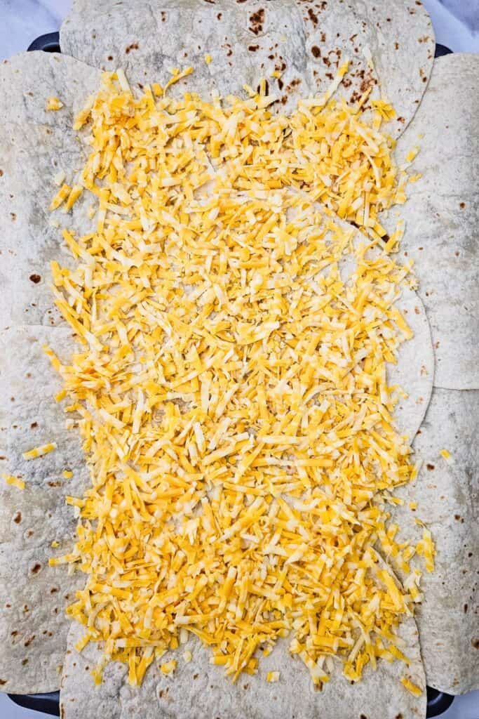 Flour tortillas layered on a sheet pan and topped with a generous amount of shredded Colby Jack cheese, ready to be filled for oven quesadillas sheet pan. 