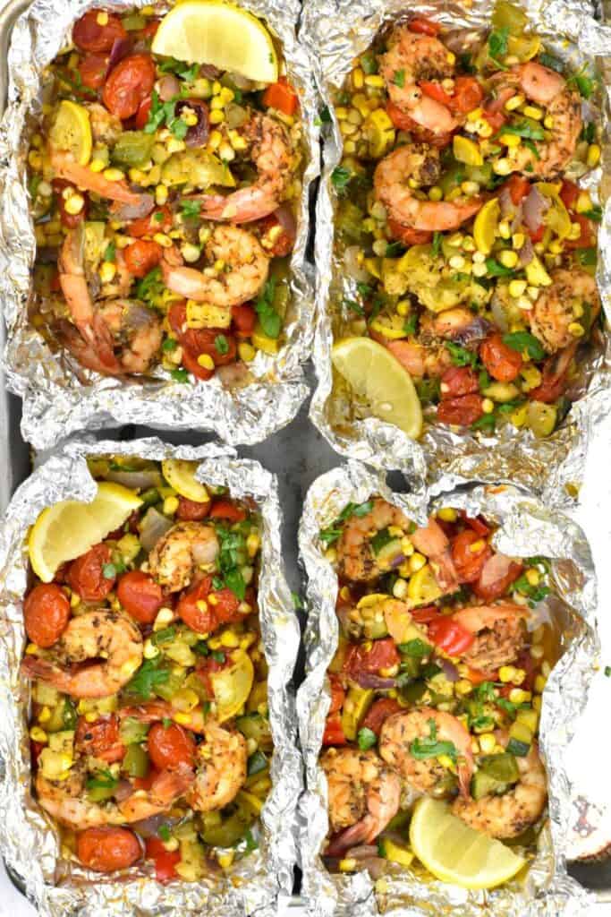 Overhead view of 4 foil packets filled with shrimp, corn, zucchini and cherry tomatoes. 