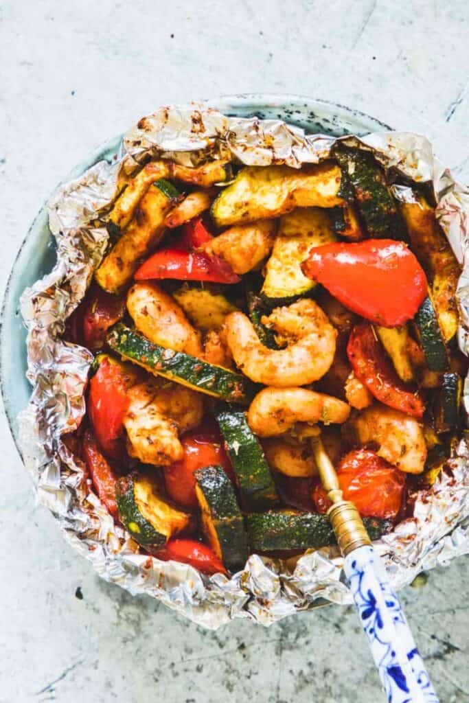 A round foil packet filled with shrimp, zucchini and red pepper.