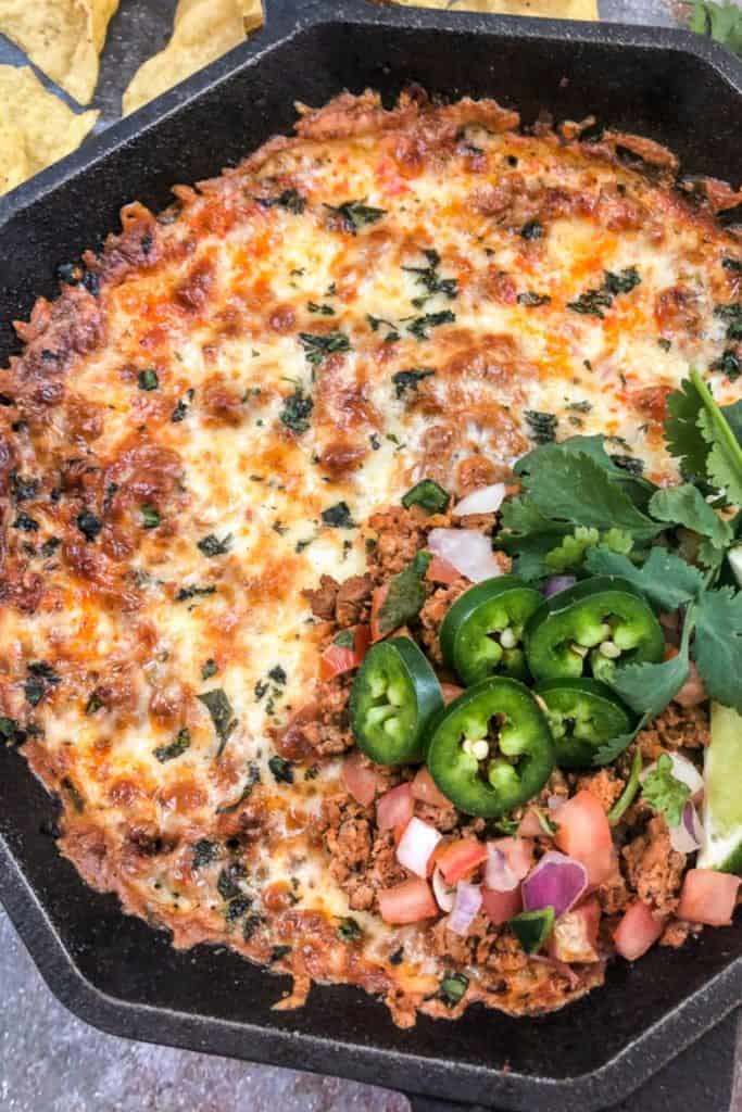 Hot Skillet Chorizo Dip baked with melted cheese and herbs, topped with fresh jalapeño slices, pico de gallo, cilantro, and lime. Served in a cast iron skillet with tortilla chips on the side for dipping.