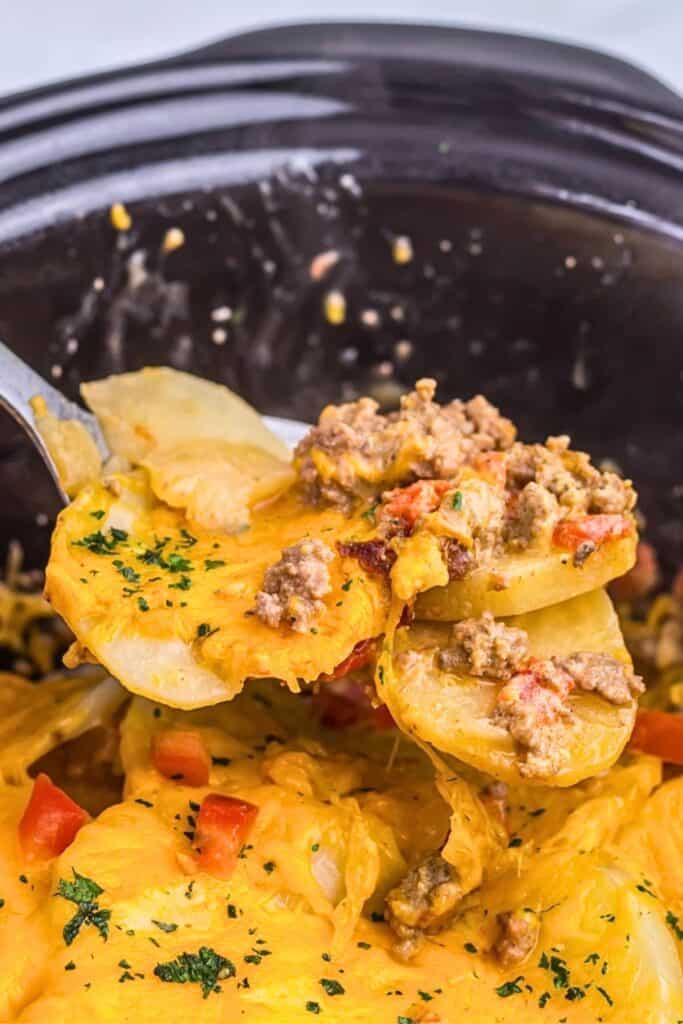 Slow cooker beef taco casserole with sliced potatoes, seasoned ground beef, diced tomatoes and melted cheddar cheese, garnished with parsley.