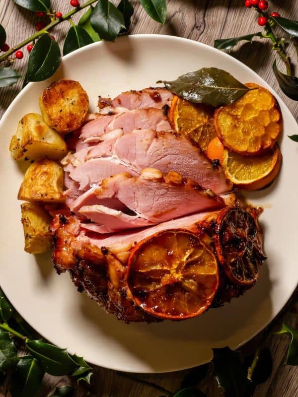 Ham coated with orange slices and roast potatoes beside.