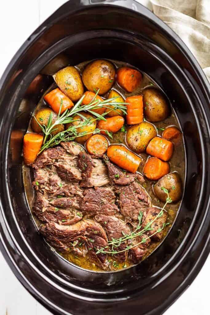 Oval slow cooker filled with beef roast, potatoes and carrots. 