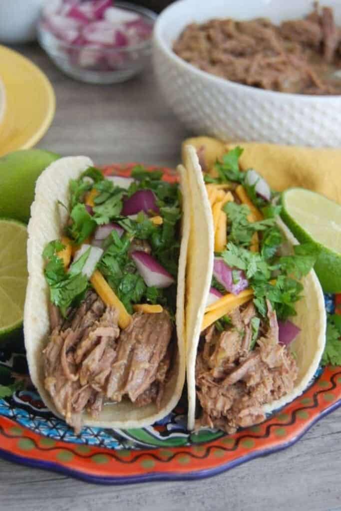 Two shredded beef tacos with cilantro, red onion and cheese on a plate. 