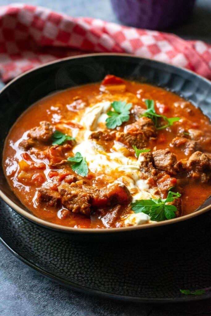 Crockpot Hungarian goulash with tender chunks of beef and peppers is served in a rich red paprika sauce. Sour cream and fresh parsley top the hearty goulash.