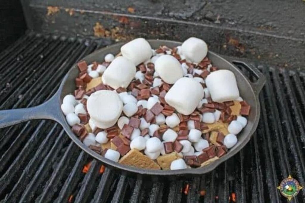 Cast iron skillet over a campfire with marshmallows, chocolate chips and graham crackers. 