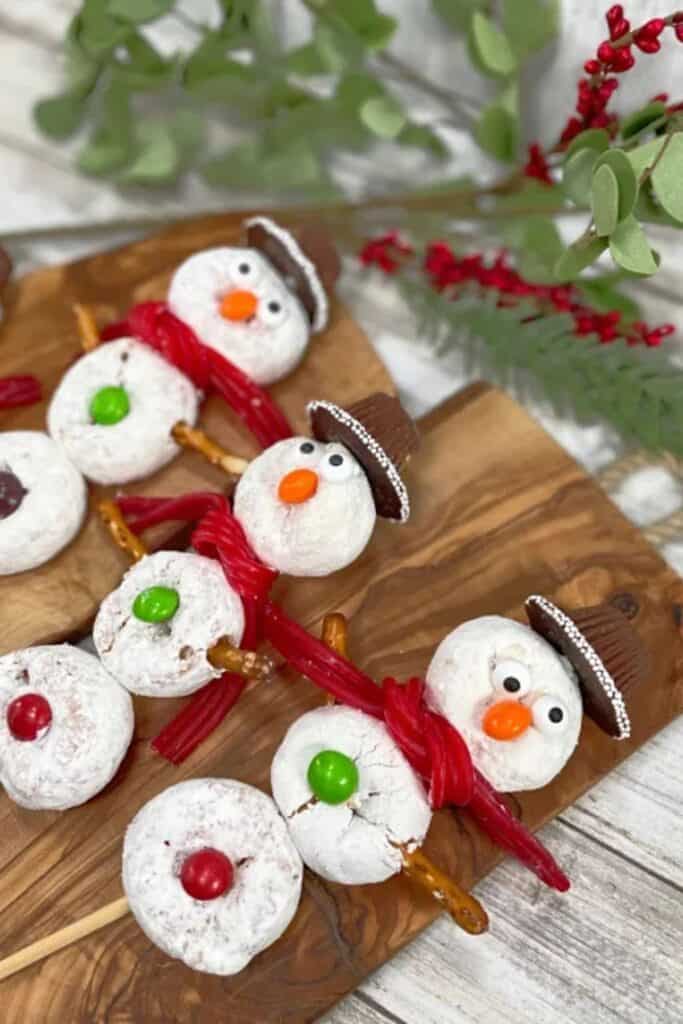 Mini donut snowmen on a stick, with chocolate hats, candy eyes & red licorice scarves.