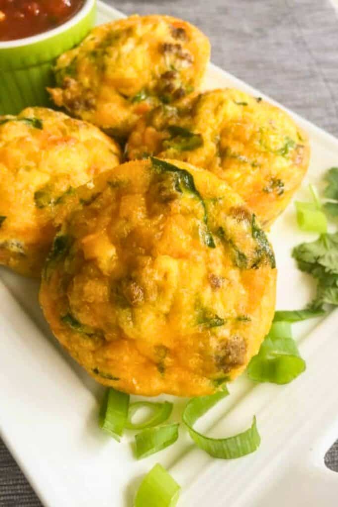 Southwestern taco egg muffins with a golden baked top filled with sausage herbs and melted cheese served on a plate with green onions and salsa.