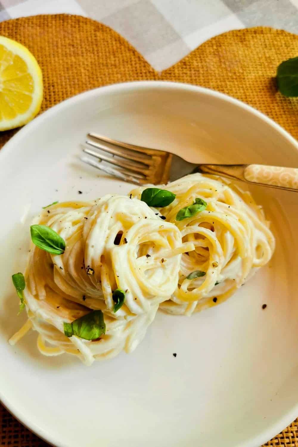 Lemon ricotta pasta with long strands of spaghetti coated in a creamy ricotta sauce and garnished with fresh basil leaves and cracked black pepper. Served in a white bowl with a lemon wedge on the side, this simple pasta dish highlights bright citrus flavors and a rich, velvety texture.