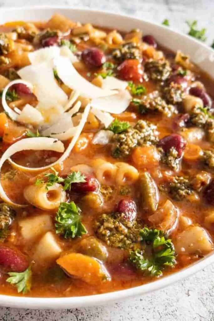 Close up of a bowl of spicy pesto minestrone topped with Parmesan slices. 