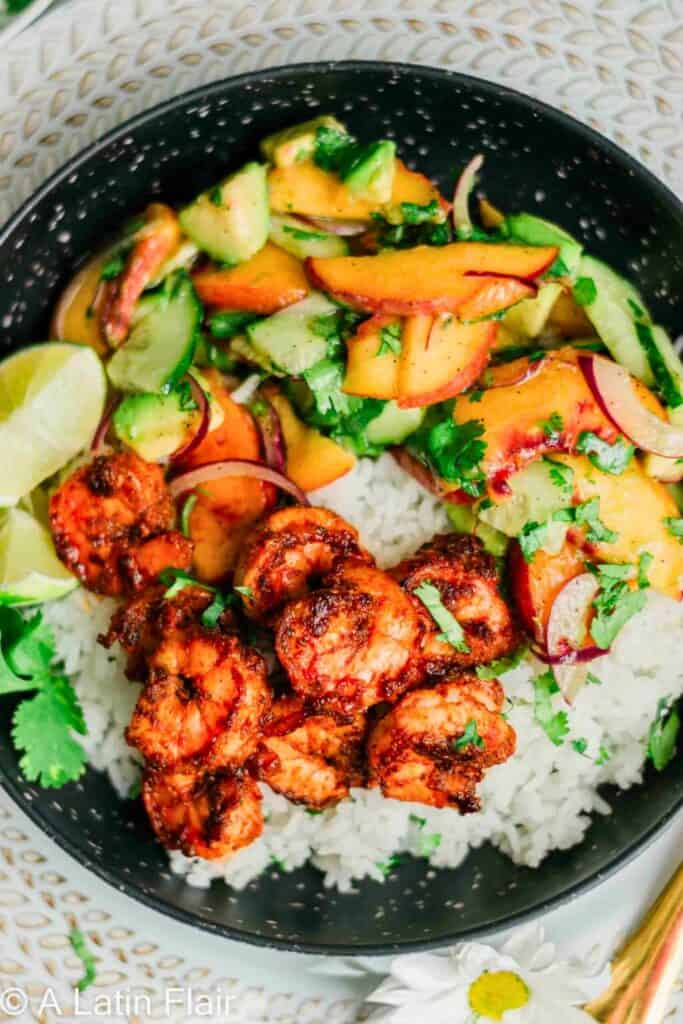 Spicy shrimp bowl with seasoned grilled shrimp served over white rice with a fresh mango cucumber salad, red onion, and cilantro. Lime wedges and bright fruit salsa add color and freshness to this spicy shrimp bowl recipe.