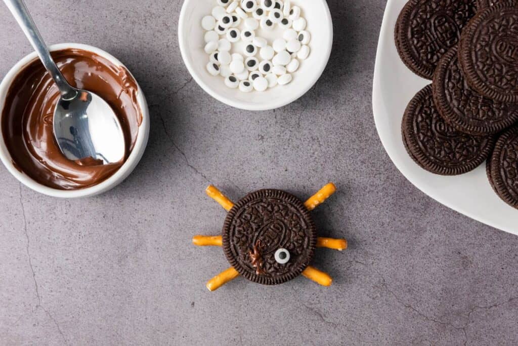 Adding candy eyes to the spider oreo with melted cholocate chips. 