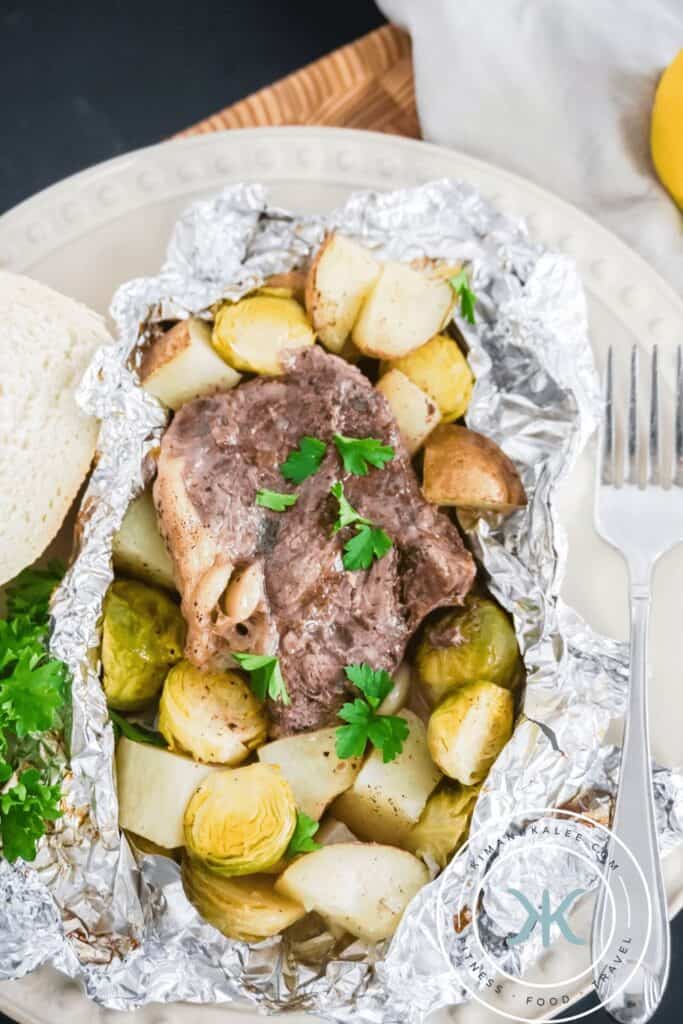 Open foil pack with steak and yellow potatoes topped with parsley garnish. 