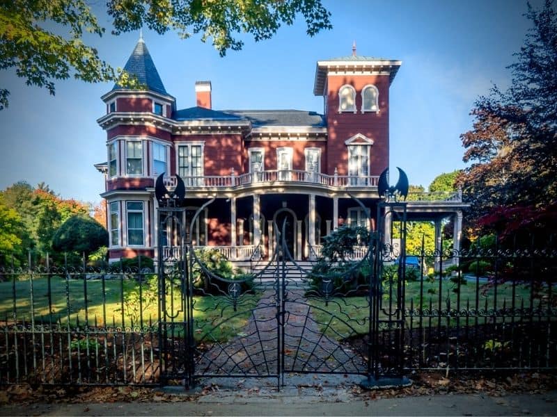 Best things to do in Maine visit Stephen Kings Victorian red Mansion with iron fence in Bangor Maine.