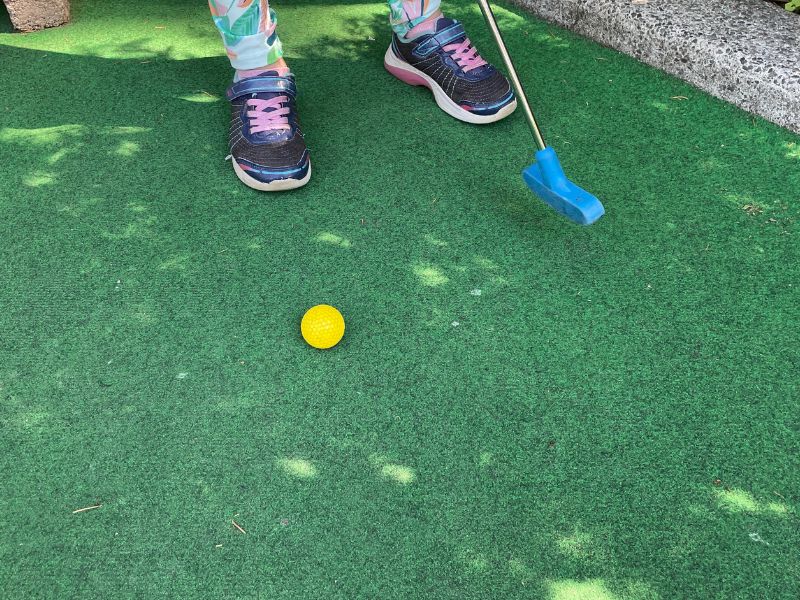 Feet with mini golf putter and ball on turf.
