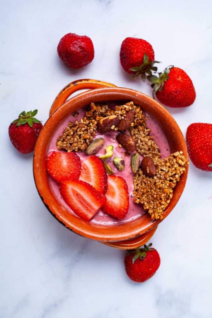 Bowl of smoothie with cut strawberries & granola on top. 