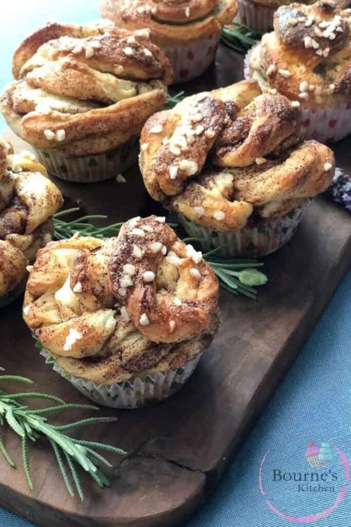 Six Swedish Connamon Buns in angled rows on a wooden cutting board, with sprigs of lavender between.