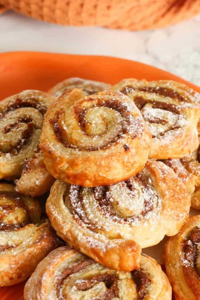 Close up of a plate piled with pumpkin pinwheels made with puff pastry.