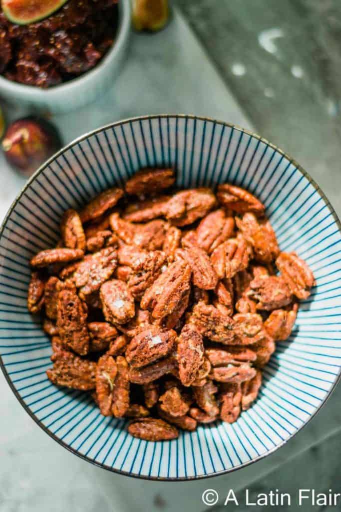 Striped bowl filled with Sweet and Spicy Pecans, coated in a glistening, caramelized seasoning blend. The glossy finish hints at both heat and sweetness, making them a flavorful snack or holiday appetizer.