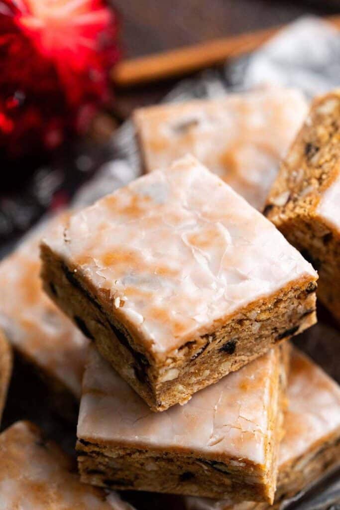 Close-up of Swiss gingerbread cookie bars stacked neatly, each topped with a smooth, glossy sugar glaze. The dense, spiced bars are studded with nuts and dried fruit.