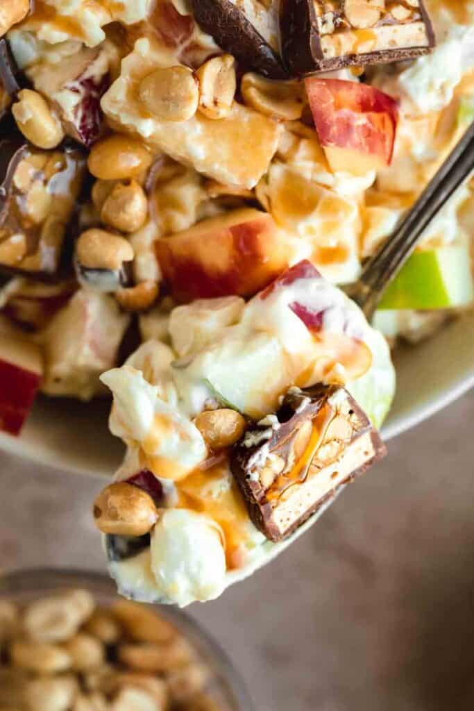 Spponful of taffy apple salad with pieces of snickers, marshmallows, apples and peanuts. 