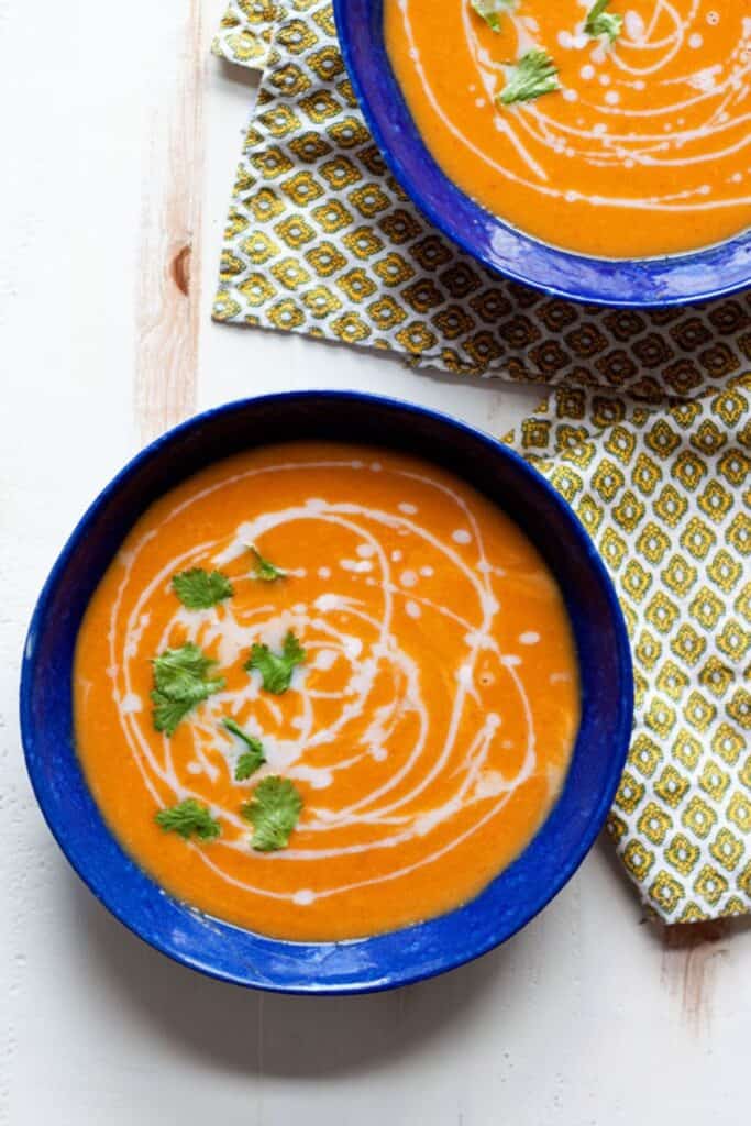 Two bowls of Thai Butternut Squash Soup drizzled with sour cream and topped with cilantro garnish.