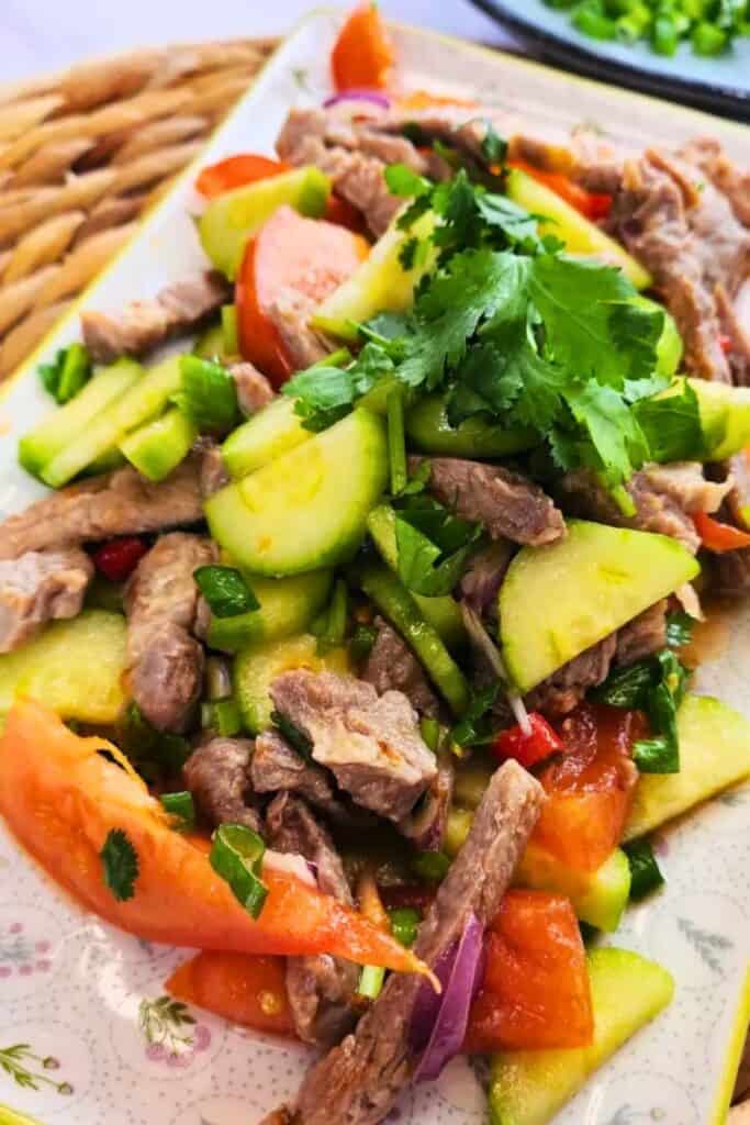Alt text: Thai grilled pork salad made with sliced grilled pork, cucumber, tomatoes, red onion, green onion, and fresh cilantro tossed in a light dressing.