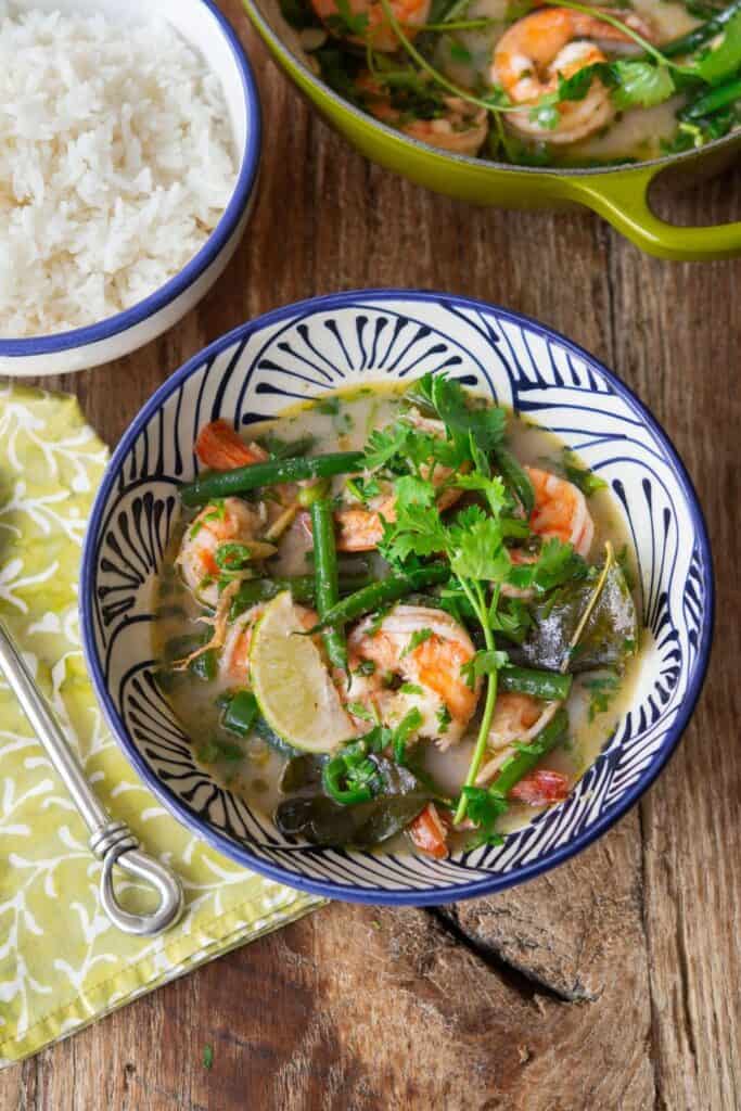 Bowl of shrimp green curry with green beans, cilantro and lime slices on top.