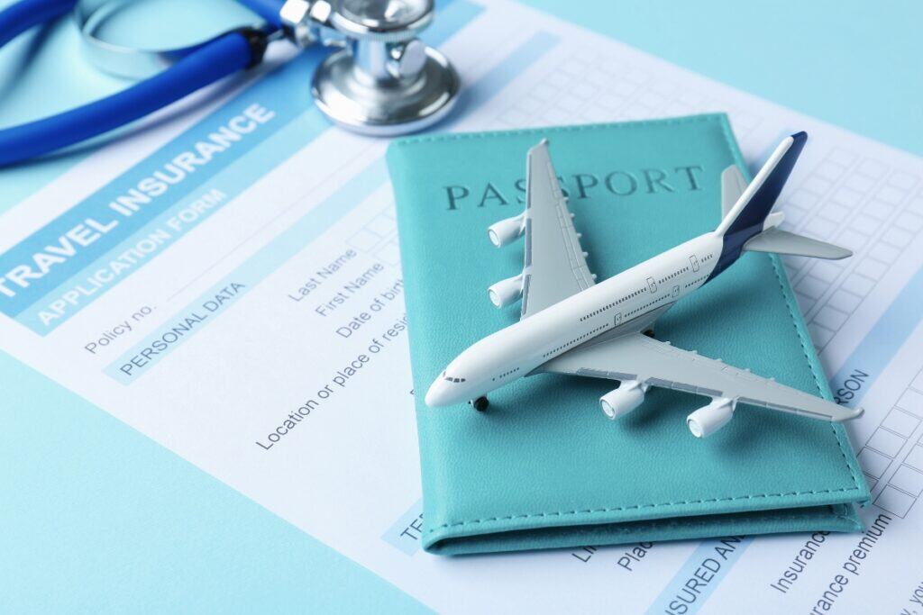 Travel medical insurance concept with a passport and model airplane resting on top of a travel insurance application form beside a stethoscope.