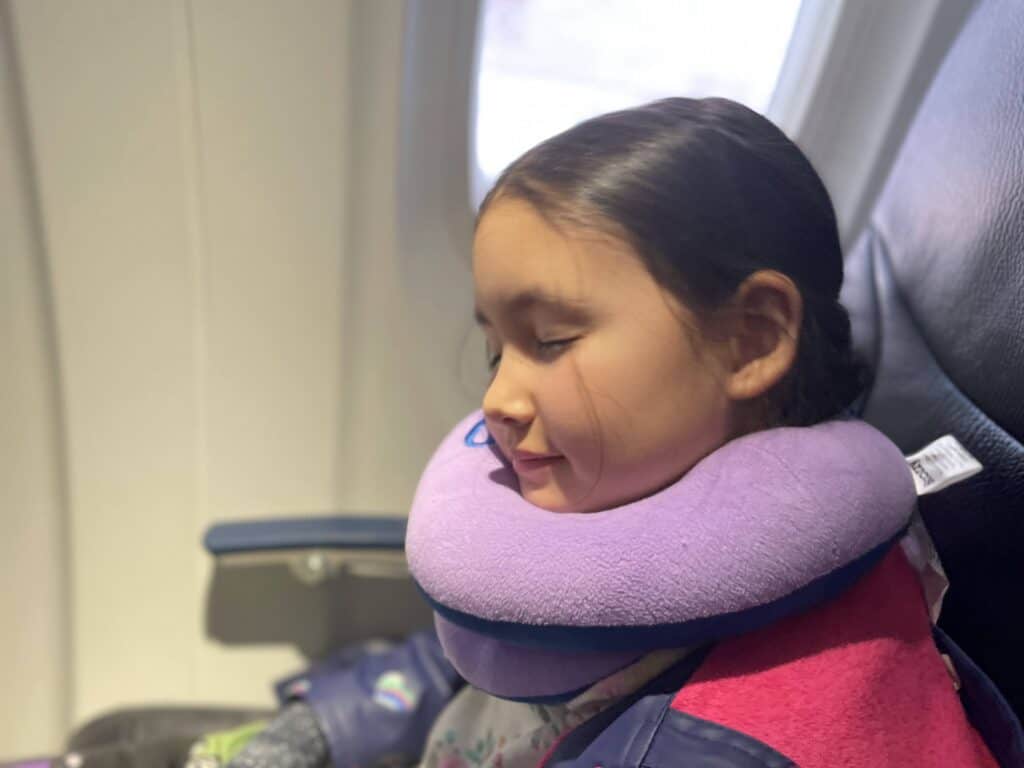 Young girl sleeping in plane with cozy travel pillow.