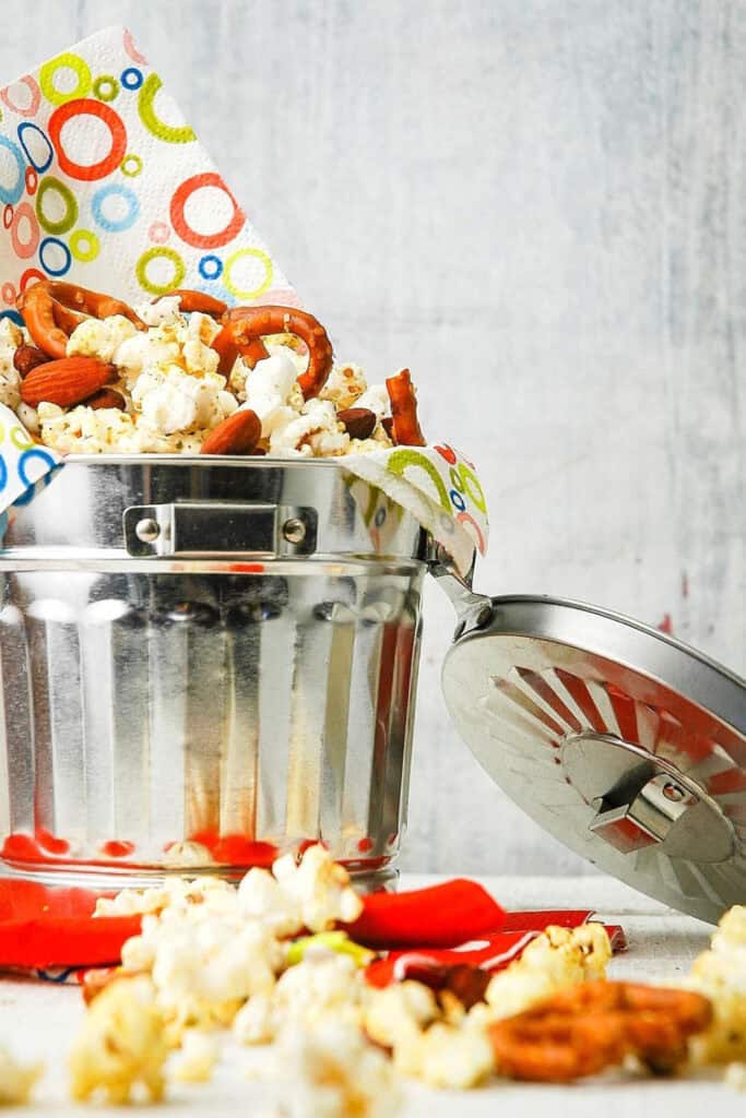 Small metal garbage can filled with popcorn, almond and pretzels snack mix. 