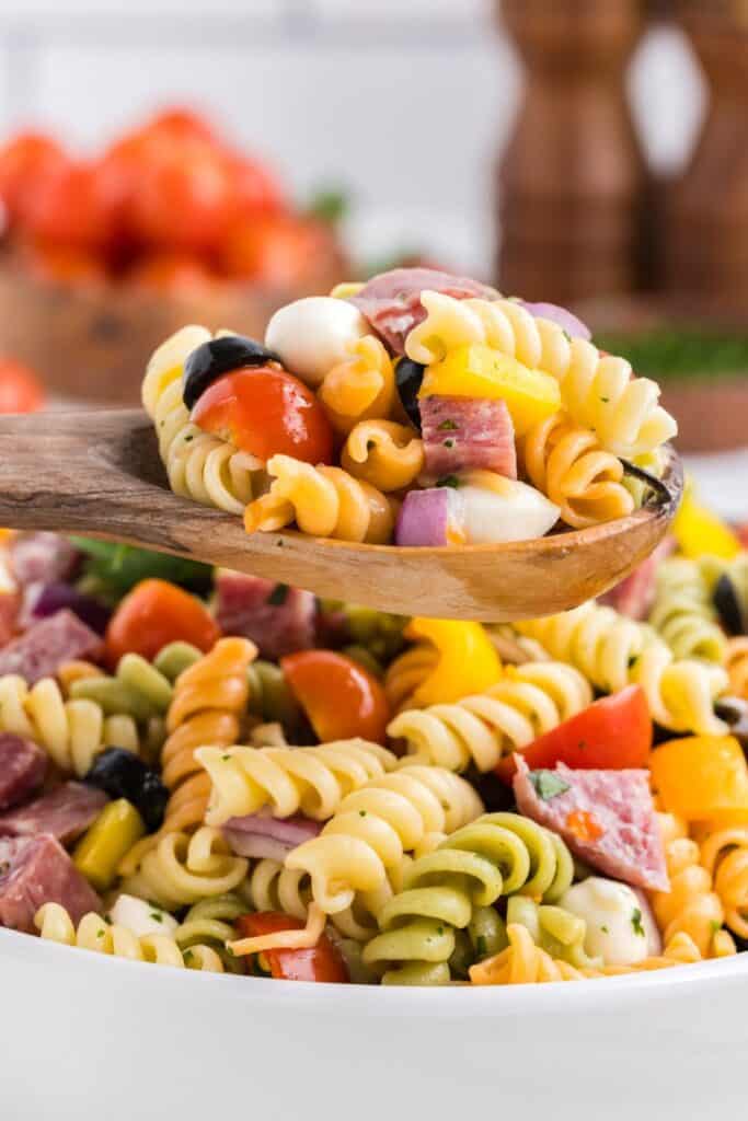 Wooden spoonful of tri-colored rotini pasta salad. 