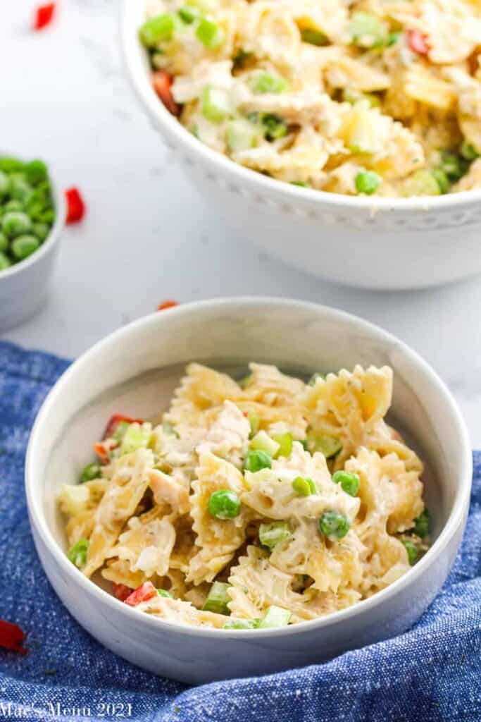 Bowl of tuna pasta salad made with bowtie pasta, flaky tuna, green peas, diced celery, and red bell pepper tossed in a creamy dressing.