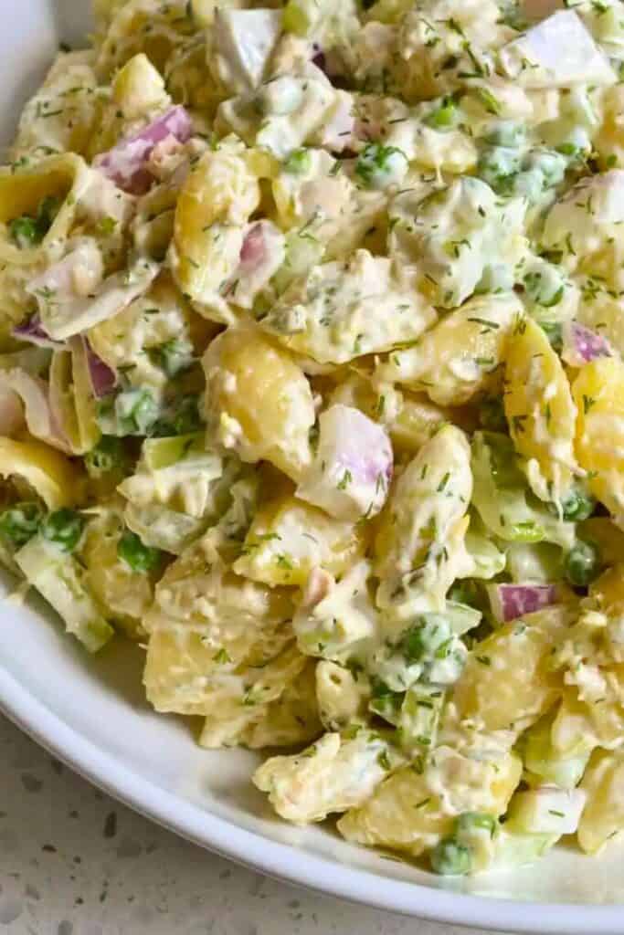 A plate of tuna pasta salad with shell pasta, tuna, peas, dill pickles, celery, and fresh dill. 