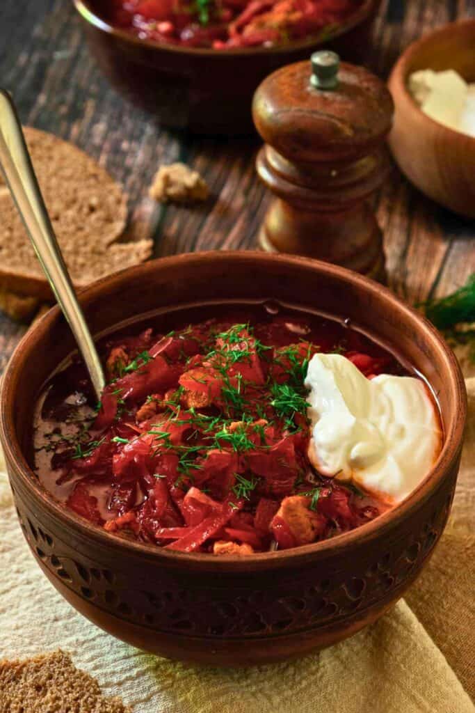Ukrainian borscht with beets cabbage and chunks of meat is served in a deep bowl with its signature rich red broth. Fresh dill and a generous dollop of sour cream top the traditional soup.