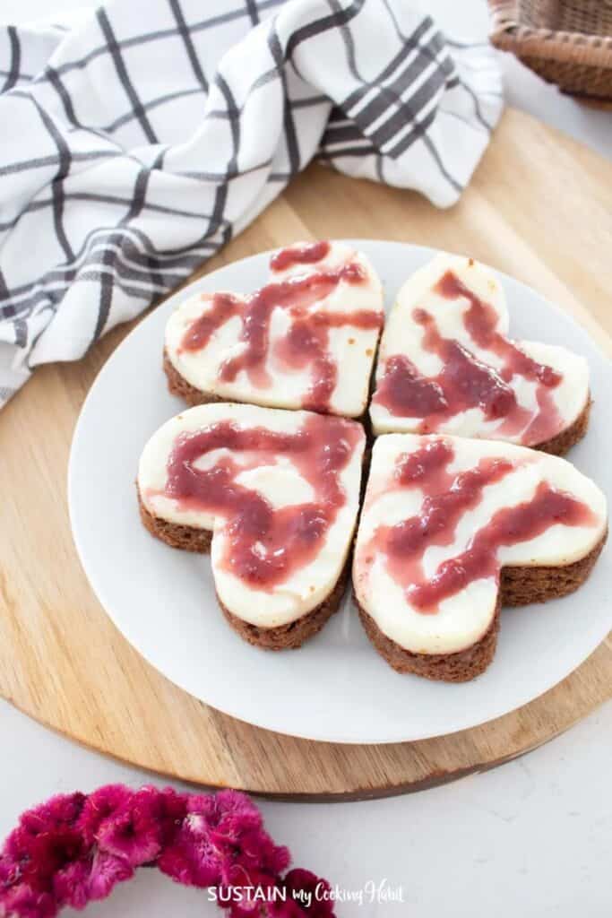 Plate of 4 heart shaped mini cakes drizzled with berry sauce. 