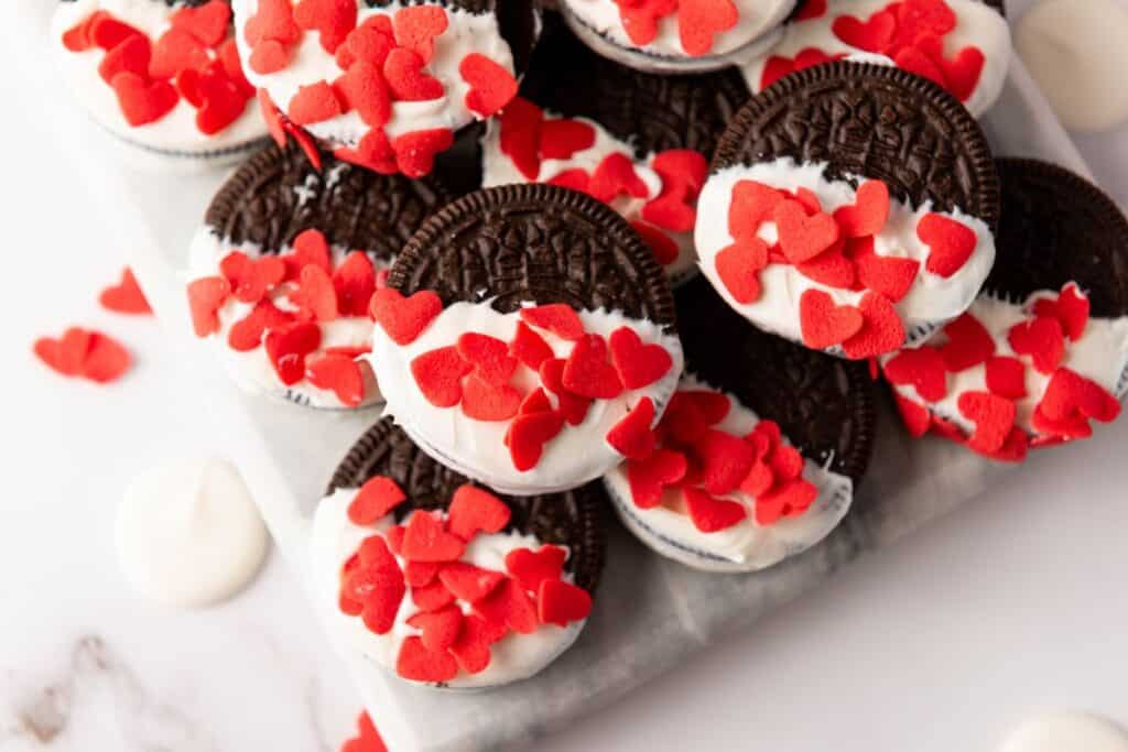 Close up of a pile of oreos half dipped in white chocolate and sprinkled with red candy hearts.