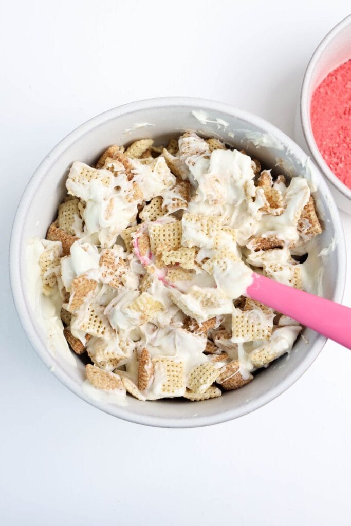 Mixing melted white chocolate with Chex cereal in a medium sized bowl. 