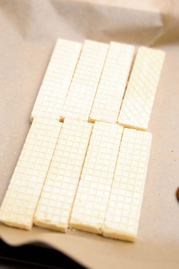 Plain vanilla wafer cookies arranged in neat rows on a sheet of parchment paper, prepped and ready for dipping or decorating as part of a holiday treat recipe. The wafers have a light color and a classic crisscross texture.