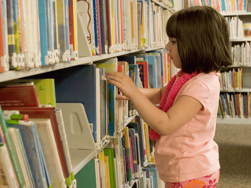 Young girl finding books at a public library. 