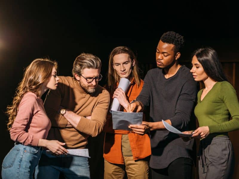 Multiethnic actors reading a screenplay on stage in a theatre.