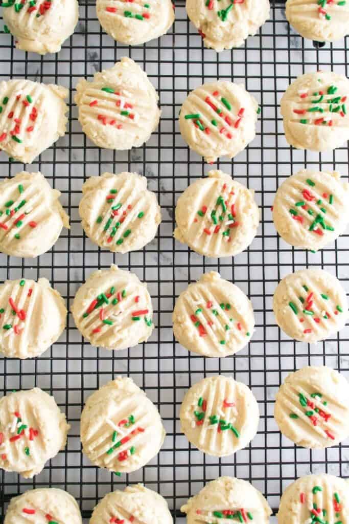 Rows of soft whipped Christmas shortbread cookies are topped with red, green, and white sprinkles and arranged neatly on a cooling rack.