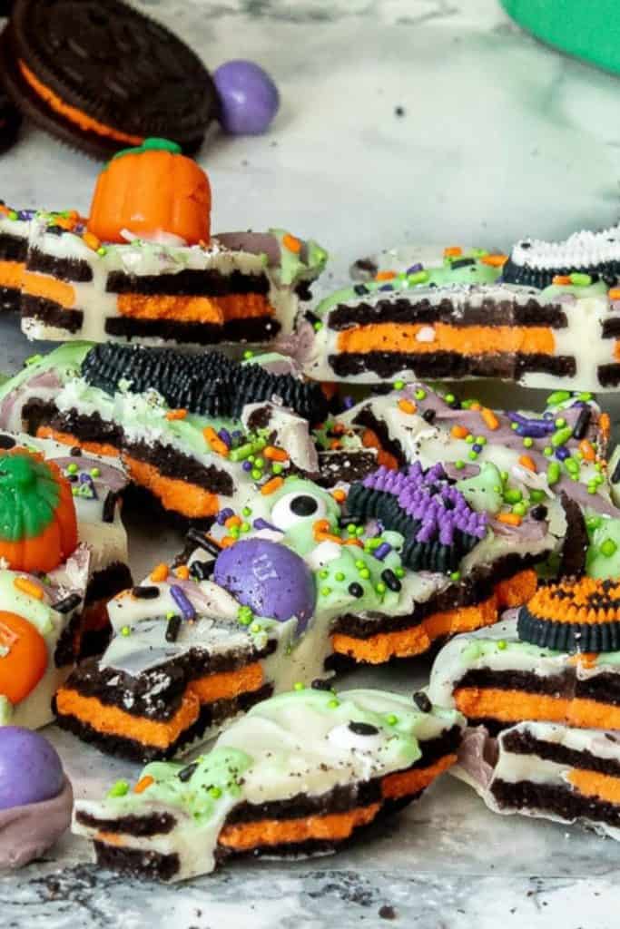 Close-up of festive Halloween bark made with crushed orange-filled chocolate sandwich cookies coated in white chocolate and topped with candy eyeballs, sprinkles, candy pumpkins, and colorful chocolate candies.