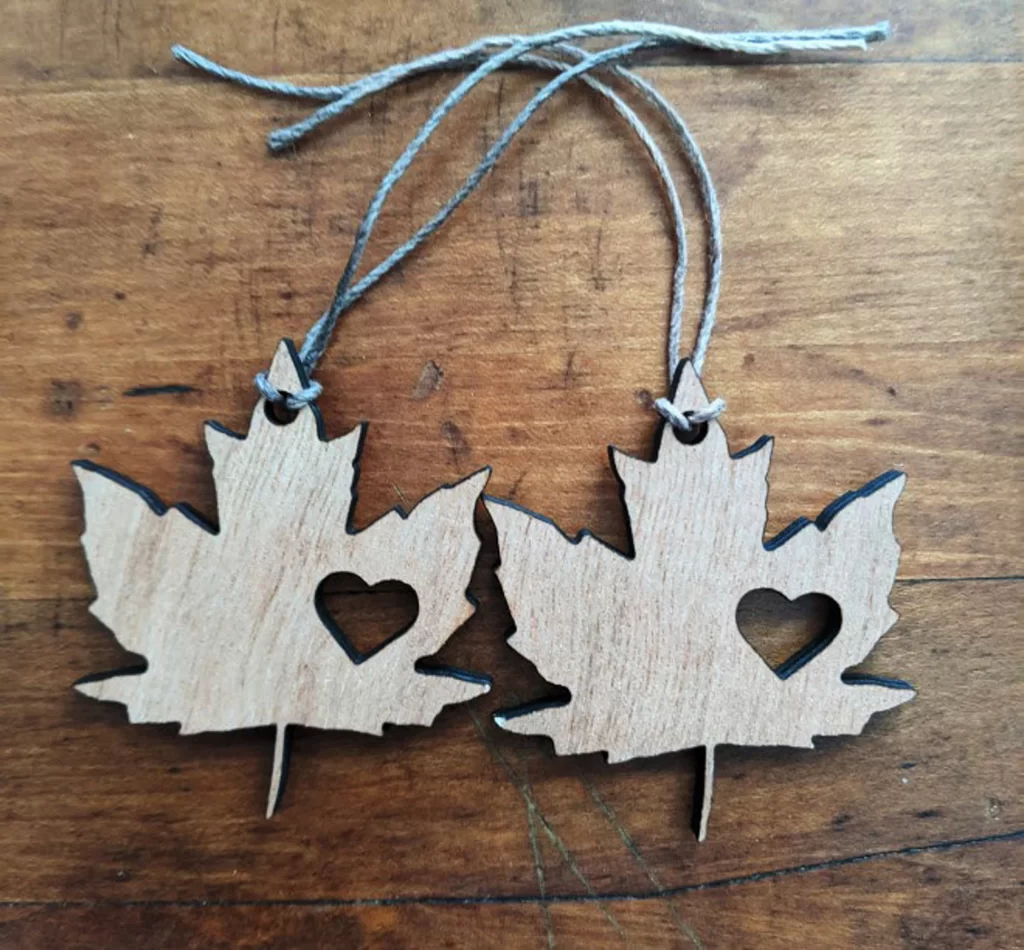 Two wooden maple leaf ornaments with a heart cut out, against a wood background.