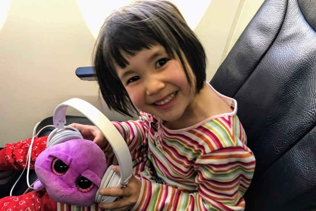 Young girl on a plane putting headphones on her stuffy.