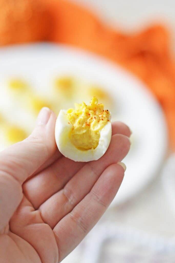 A hand holds one of the yummy egg bites with creamy yellow filling and a sprinkle of smoked paprika.