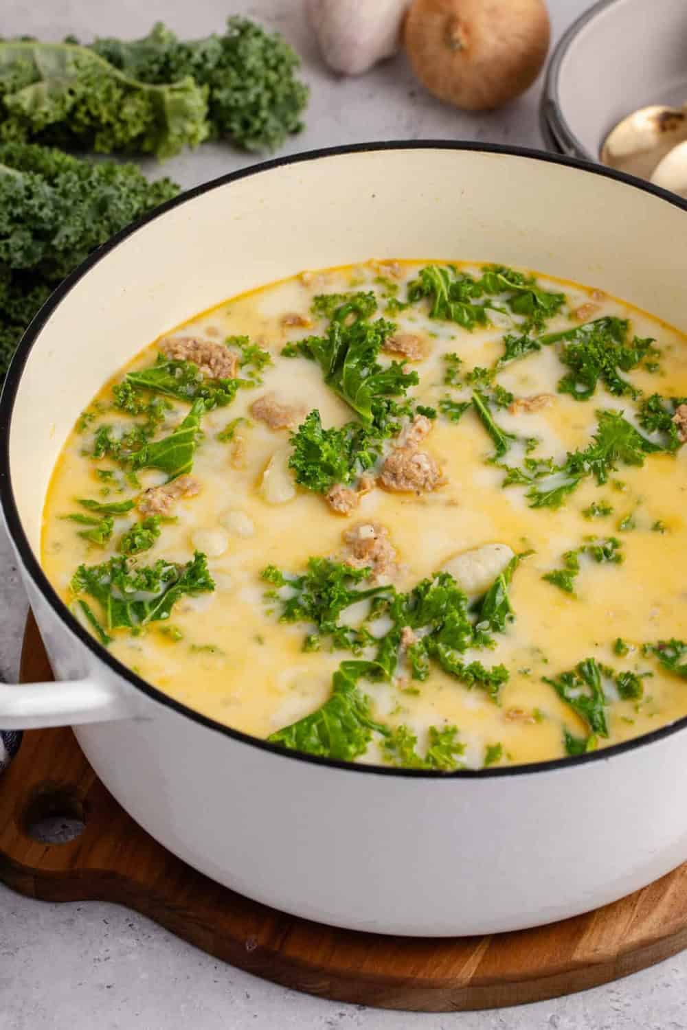 Zuppa Toscana soup with Italian sausage potatoes and curly kale simmers in a creamy broth. The hearty soup fills a large white Dutch oven ready for serving.