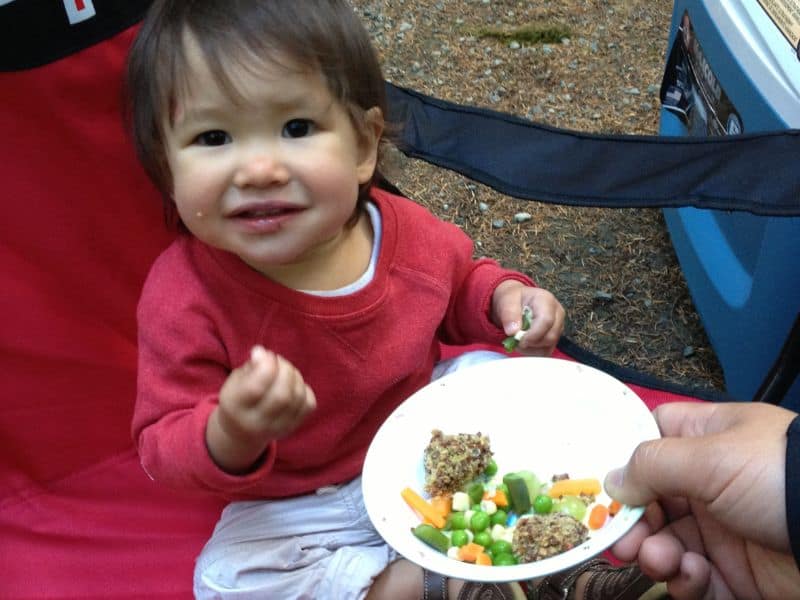 Toddler sitting in camp chair eating vegetables and meatballs