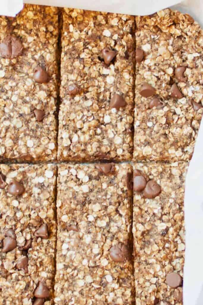 Oatmeal chocolate chip breakfast bars cut into neat rectangles, showing a dense texture packed with rolled oats and dotted with semi sweet chocolate chips. The bars are arranged closely together, highlighting their chewy consistency and lightly golden brown color.