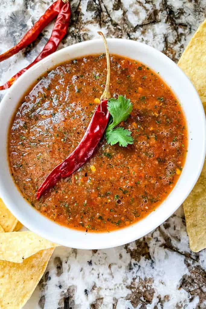Spicy Salsa Chile de Arbol in a white bowl, garnished with a whole dried chile and fresh cilantro, surrounded by tortilla chips.